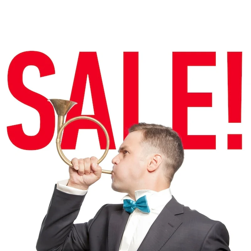 Mężczyzna w niebieskiej muszce dmuchający do fajki z napisem "sprzedaż