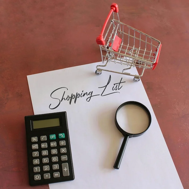 Kalkulator koszyka na zakupy z lupą i papierem z napisem "LISTA ZAKUPÓW