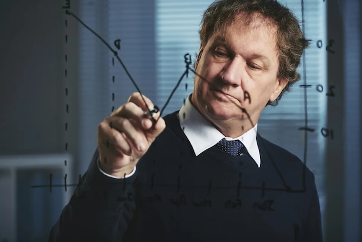 Dyrektor sprzedaży analizuje wykres sprzedaży na szklanej tablicy