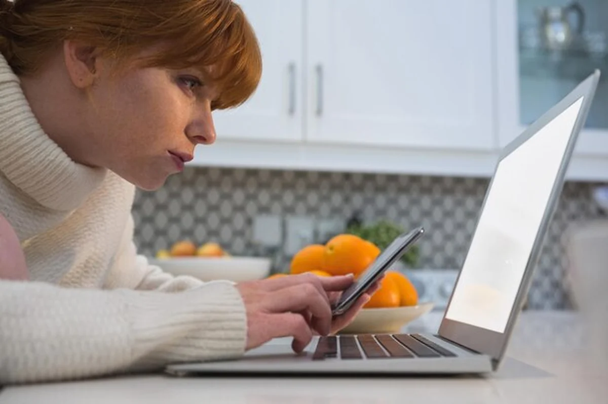 Kobieta używająca telefonu i laptopa w kuchni