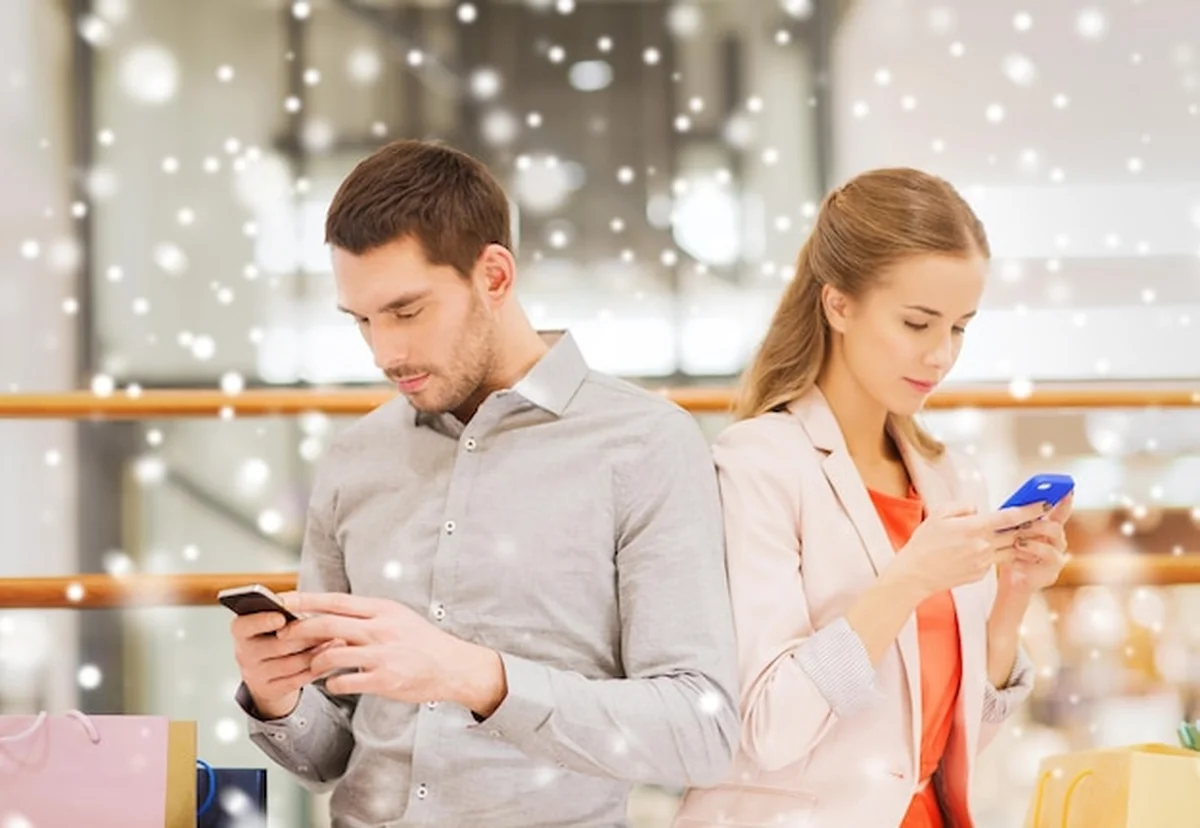 Młoda para z torbami na zakupy i smartfonami w centrum handlowym z efektem śniegu